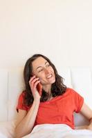 Eine Frau sitzt auf einem Bett und telefoniert foto