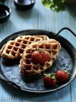 Blick aus der Vogelperspektive auf Croffle, moderne Speisen zum Mitnehmen oder Lieferservice, serviert mit Erdbeeren auf dem Vintage-Teller und blauem Tisch. foto