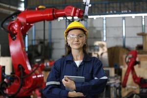 Diverse multikulturelle Ingenieure und Arbeiter der Schwerindustrie in einheitlichen Check-Automatik-Roboterarmen für die Verwendung in der Fabrik. Weiblicher Industrieunternehmer verwendet einen Tablet-Computer. foto