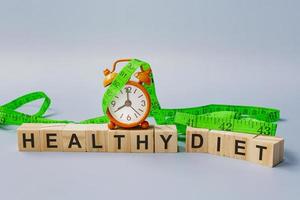 gesunder Ernährungstext auf Holzblockwürfel mit Messhahn und orangefarbener Uhr. foto