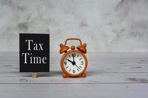 Steuerzeittext auf schwarzem Notizblock und Wecker auf 10 Uhr auf Holzschreibtisch. foto