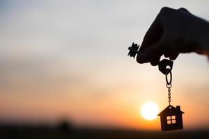 Silhouette einer Hausfigur mit einem Schlüssel, einem Stift mit einem Schlüsselbund auf dem Hintergrund des Sonnenuntergangs. Sie träumen von einem Haus, Bauen, Umzug in ein neues Haus, Hypotheken, Mieten und Kaufen von Immobilien foto