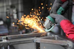 Schweißer verwendet Schleifstein auf Stahl in Fabrik mit Funken, Schweißprozess in der Industriewerkstatt, Hände mit Instrument im Rahmen. foto