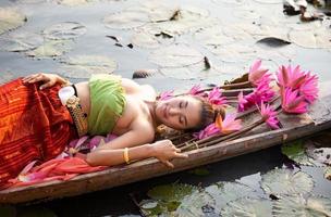 junge asiatische frauen in traditioneller kleidung im boot und rosa lotusblumen im teich. schöne mädchen in traditioneller tracht. thailändisches mädchen im retro-thailändischen kleid, thailändisches mädchen im traditionellen kostüm foto