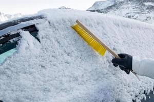 hand mit bürste, die schnee auf der windschutzscheibe des autos fegt foto