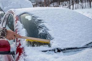 hand mit bürste, die schnee auf der windschutzscheibe des autos fegt foto