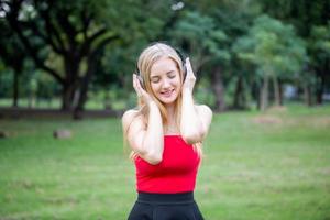 schöne blonde frau, die steht, während sie musik über kopfhörer im park hört. foto