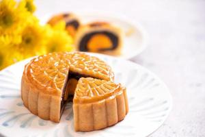 Mid-Autumn Festival traditionelles Essenskonzept - schön geschnittener Mondkuchen auf blauer Musterplatte auf weißem Hintergrund mit Blume, Nahaufnahme, Kopierraum foto