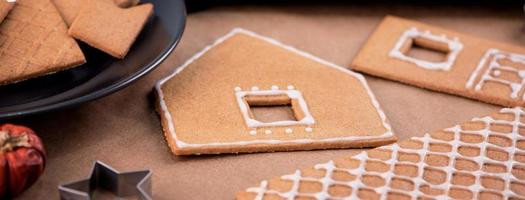 Frau dekoriert Lebkuchenhaus mit weißem Zuckerguss auf Holztischhintergrund, Backpapier in der Küche, Nahaufnahme, Makro. foto