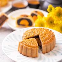 Mid-Autumn Festival traditionelles Essenskonzept - schön geschnittener Mondkuchen auf blauer Musterplatte auf weißem Hintergrund mit Blume, Nahaufnahme, Kopierraum foto