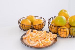 Schöne geschälte Mandarinen in einem Teller und Metallkorb isoliert auf einem hellweißen, sauberen Tisch in einer modernen, zeitgenössischen Kücheninsel, Nahaufnahme. foto