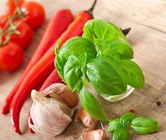 rote Chilischoten, Tomaten, Knoblauch und Basilikum auf Holzhintergrund foto