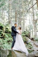 attraktives Paar Jungvermählten, glücklicher und freudiger Moment. mann und frau in festlicher kleidung sitzen auf den steinen in der nähe der hochzeitsdekoration im boho-stil. Zeremonie im Freien. foto