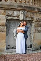 Hochzeitsfotosession auf dem Hintergrund des alten Gebäudes. der bräutigam sieht seiner braut beim posieren zu. rustikale oder Boho-Hochzeitsfotografie. foto