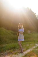 Porträt eines jungen schönen Mädchens in einem Sommerkleid. sommerfotosession im park bei sonnenuntergang. Ein Mädchen sitzt unter einem Baum im Schatten. foto