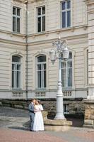 Hochzeitsfotosession auf dem Hintergrund des alten Gebäudes. der bräutigam sieht seiner braut beim posieren zu. rustikale oder Boho-Hochzeitsfotografie.