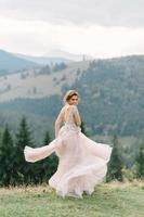 wirbelnde Braut, die Schleierrock des Hochzeitskleides am Kiefernwald hält foto