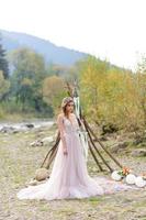 glückliche Braut in einem rosa Hochzeitskleid. das mädchen hält einen hochzeitsstrauß in ihren händen. Hochzeitszeremonie im Boho-Stil im Wald. foto