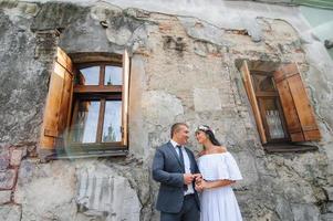 Hochzeitsfotosession auf dem Hintergrund des alten Gebäudes. der bräutigam sieht seiner braut beim posieren zu. rustikale oder Boho-Hochzeitsfotografie. foto