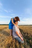 Erwachsener Bauer und Ehefrau verbringen Zeit auf dem Feld. der mann sitzt. Eine Frau steht neben ihm und umarmt ihn. Eine Frau küsst ihren Mann auf den Kopf. foto