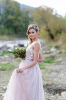 glückliche Braut in einem rosa Hochzeitskleid. das mädchen hält einen hochzeitsstrauß in ihren händen. Hochzeitszeremonie im Boho-Stil im Wald. foto