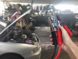 Hand, die Autobatterieladegerät über verschwommenem Auto im Garagenhintergrund hält foto