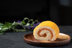 Orangenrollenkuchen in Holzplatte auf schwarzem Hintergrund foto