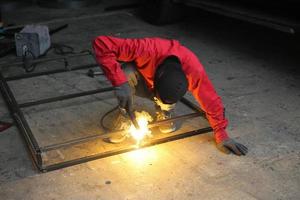 Schweißer verwendet Schleifstein auf Stahl in Fabrik mit Funken, Schweißprozess in der Industriewerkstatt, Hände mit Instrument im Rahmen. foto