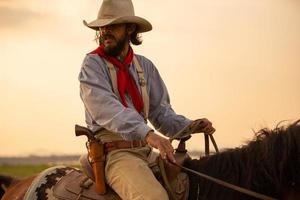 Cowboy zu Pferd vor einem wunderschönen Sonnenuntergang, Cowboy und Pferd im ersten Licht, Berg, Fluss und Lifestyle mit natürlichem Lichthintergrund