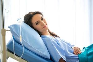 porträt einer jungen patientin, die auf einem klinikbett liegt und ein krankenhauskleid trägt. foto