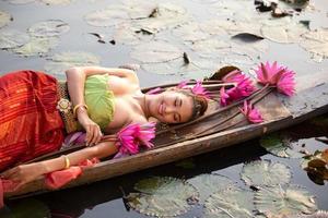 junge asiatische frauen in traditioneller kleidung im boot und rosa lotusblumen im teich. schöne mädchen in traditioneller tracht. thailändisches mädchen im retro-thailändischen kleid, thailändisches mädchen im traditionellen kostüm foto