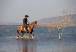 Cowboy zu Pferd vor einem wunderschönen Sonnenuntergang, Cowboy und Pferd im ersten Licht, Berg, Fluss und Lifestyle mit natürlichem Lichthintergrund foto