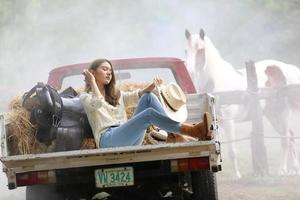 Cowgirl-Model posiert auf dem Bauernhof. ein Porträt eines schönen jungen Cowgirls, das sich in einem Stall auf einer Farm an eine Wand lehnt. foto