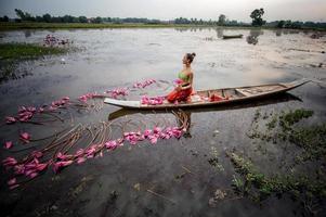 junge asiatische frauen in traditioneller kleidung im boot und rosa lotusblumen im teich. schöne mädchen in traditioneller tracht. thailändisches mädchen im retro-thailändischen kleid, thailändisches mädchen im traditionellen kostüm foto