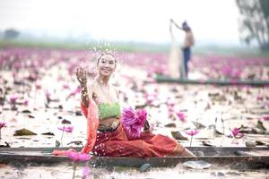 junge asiatische frauen in traditioneller kleidung im boot und rosa lotusblumen im teich. schöne mädchen in traditioneller tracht. thailändisches mädchen im retro-thailändischen kleid, thailändisches mädchen im traditionellen kostüm foto