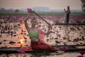 junge asiatische frauen in traditioneller kleidung im boot und rosa lotusblumen im teich. schöne mädchen in traditioneller tracht. thailändisches mädchen im retro-thailändischen kleid, thailändisches mädchen im traditionellen kostüm foto