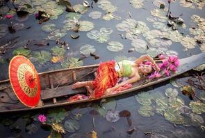 junge asiatische frauen in traditioneller kleidung im boot und rosa lotusblumen im teich. schöne mädchen in traditioneller tracht. thailändisches mädchen im retro-thailändischen kleid, thailändisches mädchen im traditionellen kostüm foto