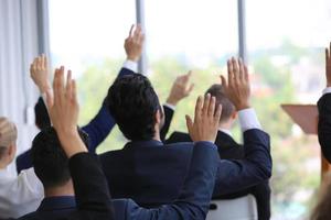 geschäftsleute im seminar heben die hand zur abstimmung bei tagungsaktivitäten oder geschäftsveranstaltungen und stellen fragen beim seminar oder workshop der sprecher foto