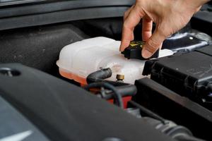 Mechaniker inspiziert den Ausgleichsbehälter mit rosafarbenem Frostschutzmittel. Fahrzeugkühlmittelstand im Kühlersystem des Autos. Autoteile foto