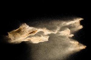abstrakte sandwolke.goldener sandspritzer vor dunklem hintergrund.gelbe sandfliegenwelle in der luft. Sand explodiert auf schwarzem Hintergrund und wirft Freeze-Stop-Motion-Konzept. foto