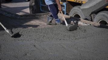 Zugeschnittenes Bild eines asiatischen Bauarbeiters, der mit einer Hacke Beton auf dem Boden auf der Baustelle verteilt foto