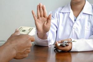 Zugeschnittenes Bild der Hand einer Ärztin, die sich weigert, Bestechungsgelder von geduldigen Männern in der Arztpraxis anzunehmen, Korruption und Bestechung im medizinischen Konzept foto