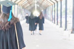 Hintergrund des Bildungskonzepts, verschwommen von der Rückansicht junger Menschen, die ihren Abschluss in Mützen und Kleidern machen, die in der Universität spazieren gehen foto