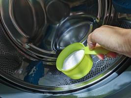 Schließen Sie die Hand, die Backpulver in die Frontlader-Waschmaschine gibt, um sie in der Waschtrommel zu reinigen. foto