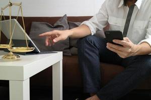 justiz und gesetz kontext. männliche anwaltshand sitzt auf sofa und arbeitet mit smartphone, digitaler tablet-computer-andocktastatur mit hammer und dokument auf lebendem tisch zu hause