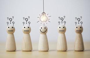 Smiley-Holzmensch mit Glühbirne und andere Menschen mit Fragezeichen für kreatives Denken und Problemlösungslösungskonzept.