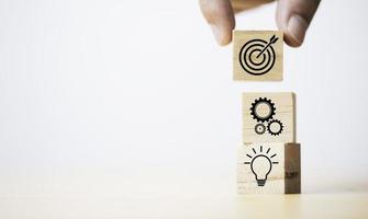 Hand setzende Zieltafel, die auf Holzwürfelblock auf mechanischem Getriebe und Glühbirnensymbol für kreatives und eingerichtetes Geschäftsziel-Zielzielkonzept gedruckt wird. foto