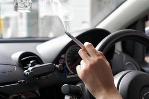 Frau mit dem Finger, der eine Zigarette und ein Lenkrad hält, während sie auf der Autobahn Auto fährt. Frauen rauchen im Auto foto