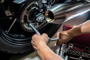 mechaniker, der einen schraubenschlüssel und eine buchse am motorradkettenrad verwendet. wartungs- und reparaturkonzept in der motorradgarage. selektiver fokus foto