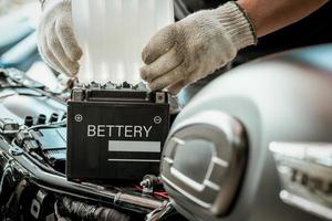 Der Mechaniker ersetzt die Motorradbatterie und hält ein Säurepaket oder ein versiegeltes Batterieelektrolytpaket, um das Auffüllen der Batterie, die Wartung des Motorrads sowie das Service- und Reparaturkonzept vorzubereiten. selektiver Fokus foto